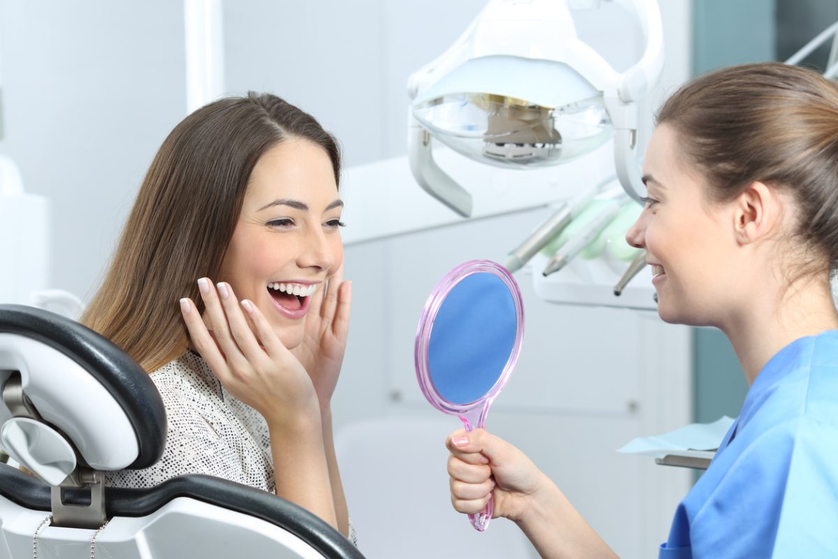 Happy dentist patient checking whitening results looking in a mirror