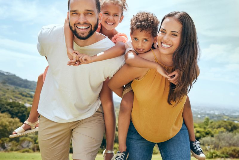 Happy family, mother and father with children on back in a nature park for bonding and relaxing in summer. Smile, mom an dad love enjoying quality time with siblings or kids outdoors for fresh air